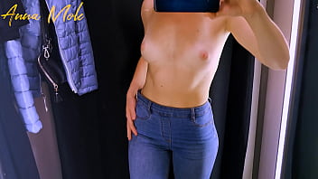 A girl in tight pants caresses small breasts in a fitting room.
